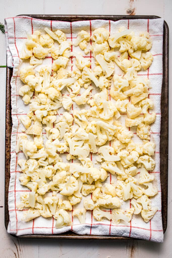 Steamed cauliflower on baking sheet lined with dish towel.