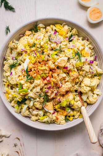 Prepared cauliflower potato salad in bowl with serving tongs.