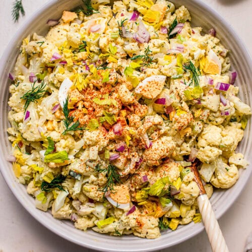 Prepared cauliflower potato salad in bowl with serving tongs.