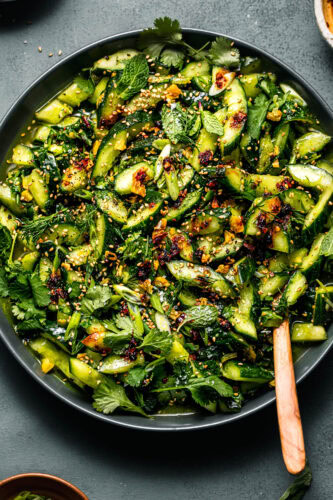 Overhead shot of smashed cucumber salad in green bowl with wooden serving spoon.