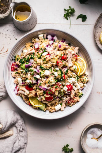 Prepared Quinoa chicken salad in white serving bowl next to small bowls of toppings.