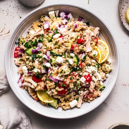 Prepared Quinoa chicken salad in white serving bowl next to small bowls of toppings.