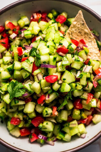 Close up of chip being dipped into fresh cucumber salsa.