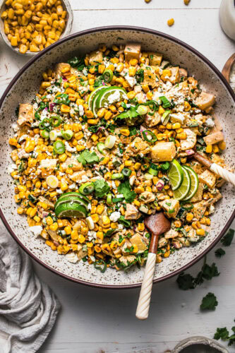 Corn potato salad in speckled bowl with tongs.