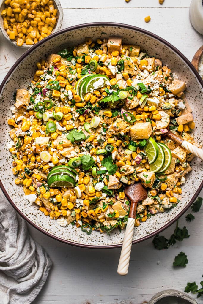 Corn potato salad in speckled bowl with tongs.