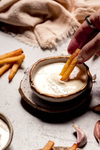 Fries dipping into bowl of garlic aioli.