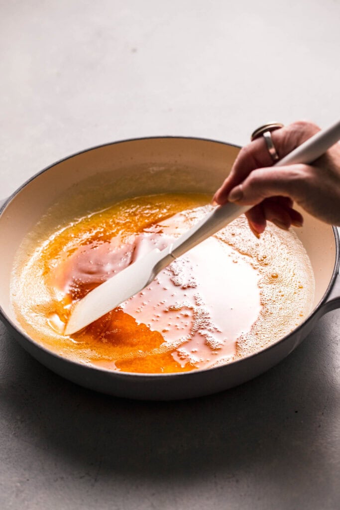 Hand stirring browned butter in skillet. 