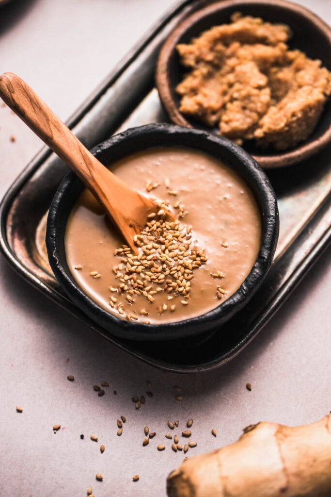 Miso sauce in small black bowl sprinkled with sesame seeds.
