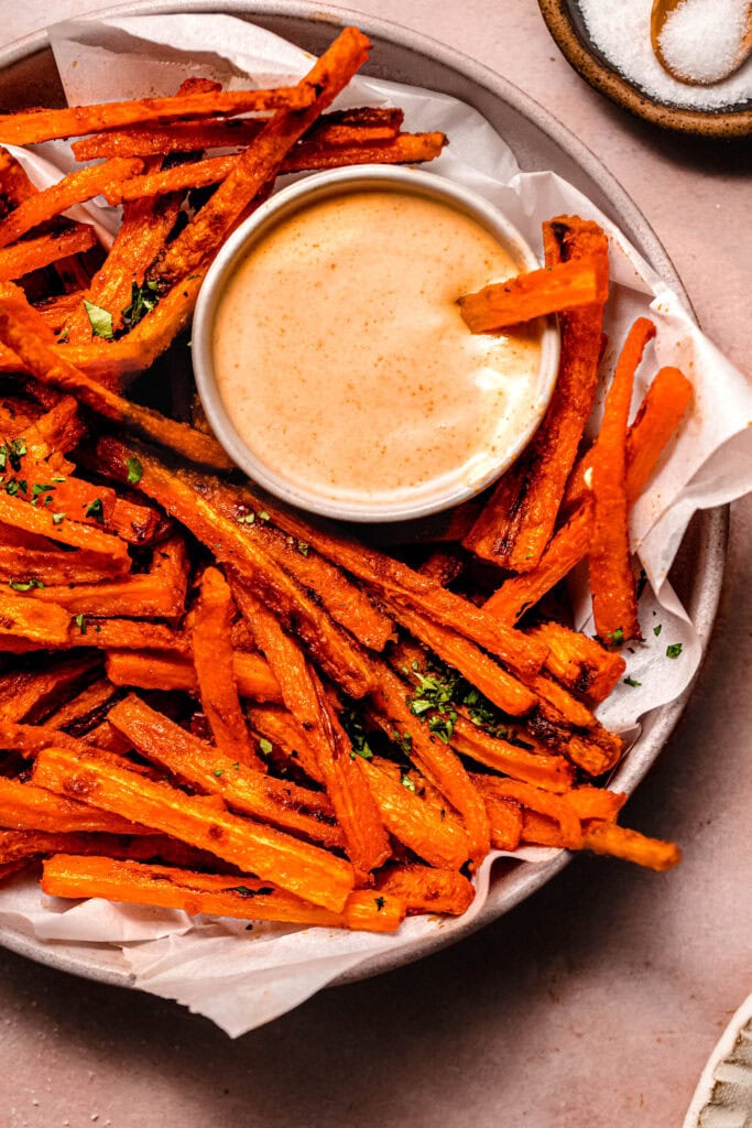 Crispy roasted carrot fries nestled in parchment, dipping into a bowl of spicy mayo sauce.