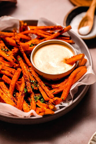 Basket of carrot fries on parchment paper paired with a vibrant sriracha mayo for dipping.