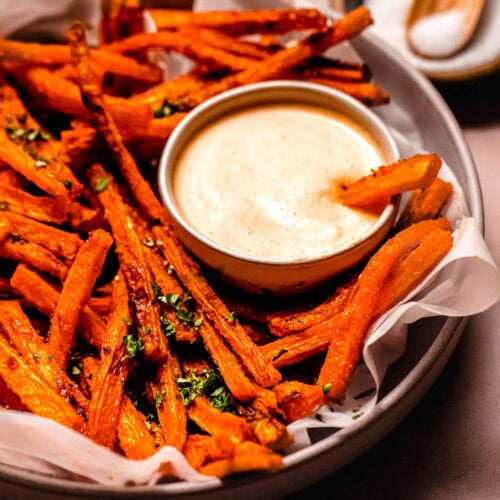 Basket of carrot fries on parchment paper paired with a vibrant sriracha mayo for dipping.