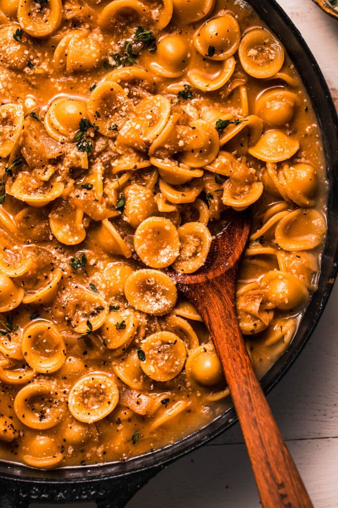 Close up of french onion pasta in skillet with wooden spoon.