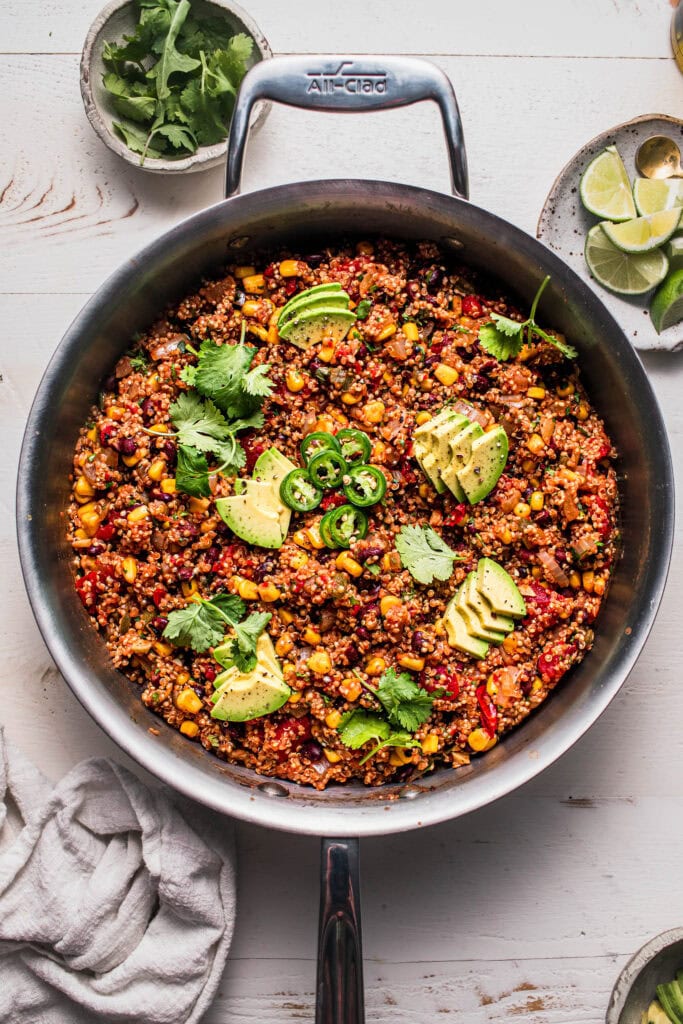 Finished mexican quinoa in skillet topped with avocado and jalapeno.