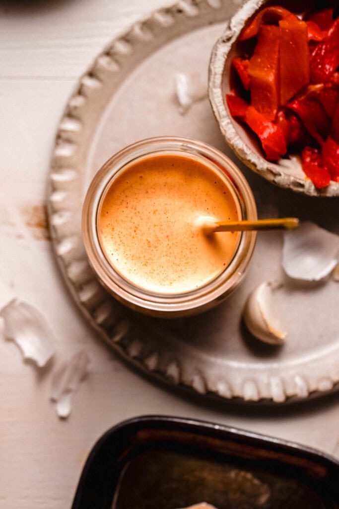 Red pepper aioli in small bowl with gold spoon.