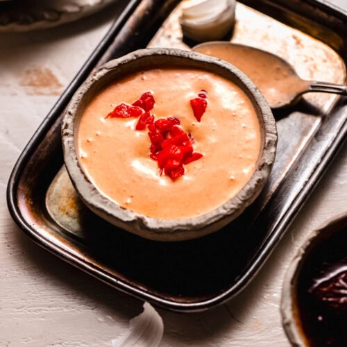 Bowl of red pepper aioli topped with chopped roasted red peppers.