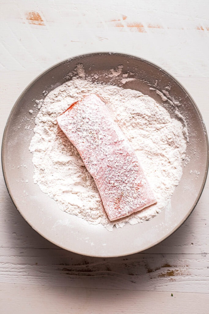Salmon filet being dredged in flour.