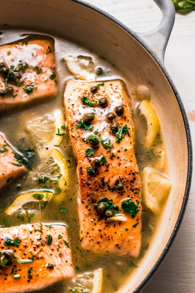 Salmon filet flecked with capers and lemon sauce in skillet.