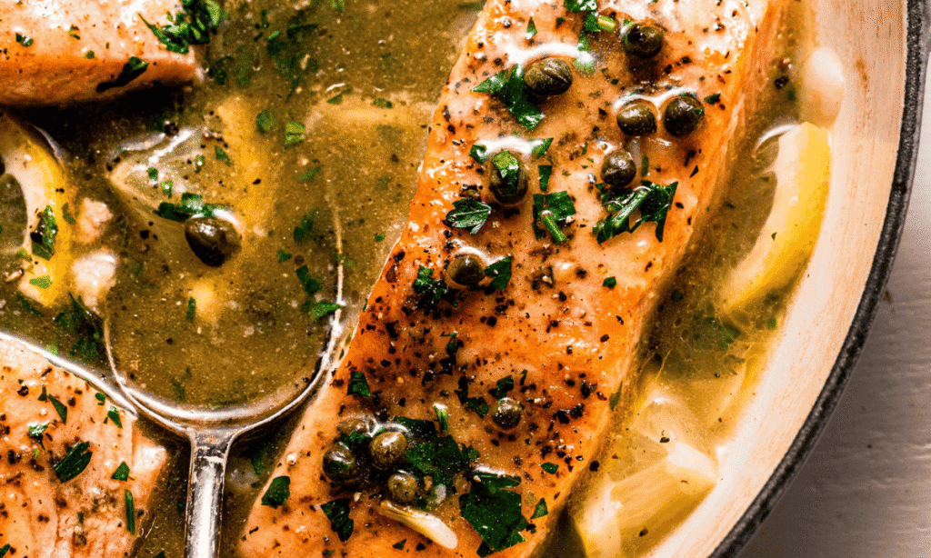 Close up of piccata sauce being spooned over salmon. 