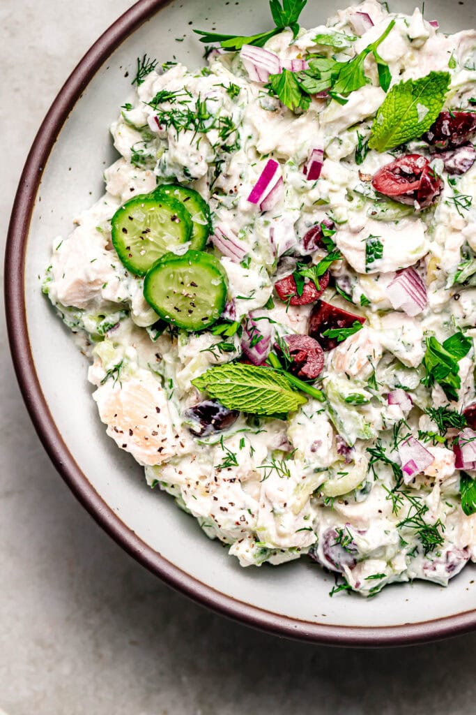 Overhead close up of finished tzatziki chicken salad in bowl topped with cucumbers and mint sprig.