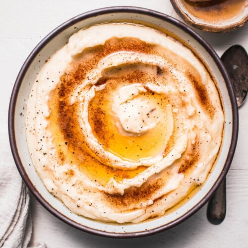 Finished browned butter mashed potatoes in serving bowl drizzled with brown butter swirl.