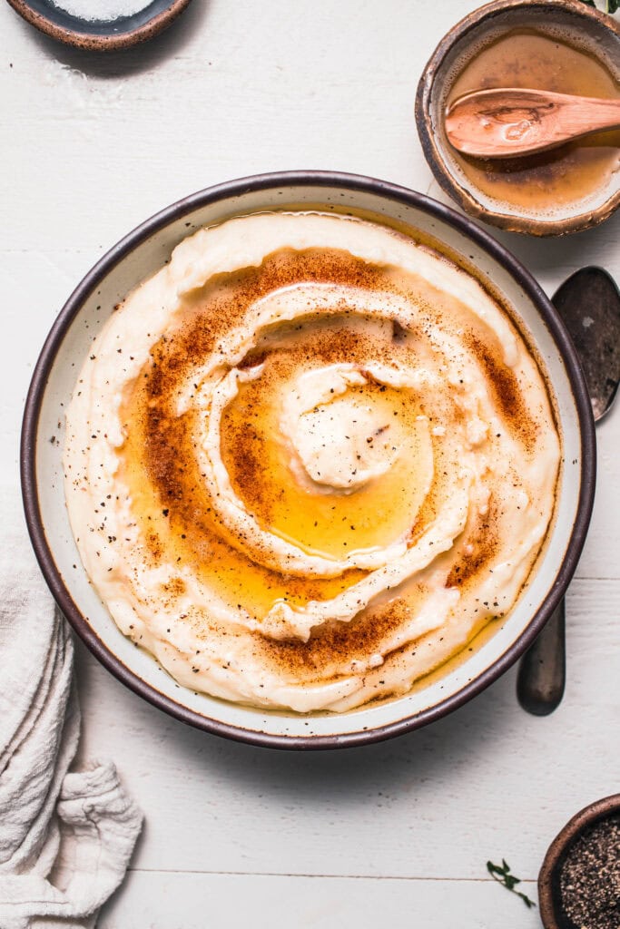 Finished browned butter mashed potatoes in serving bowl drizzled with brown butter swirl.