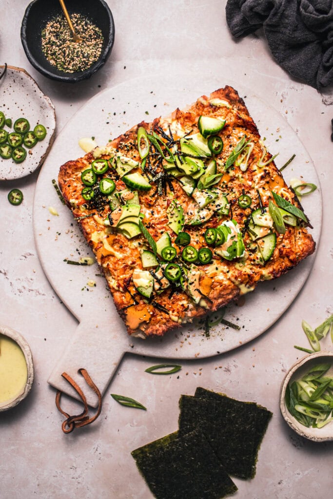 Sushi bake on cutting board garnished with avocados, nori and serrano peppers.
