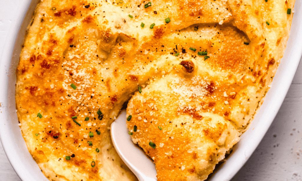 Horizontal image of smoked gouda mashed potatoes in baking dish with serving spoon.