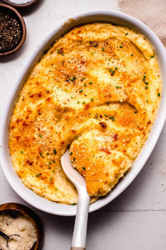 Overhead shot of finished smoked gouda mashed potatoes in baking dish with serving spoon.