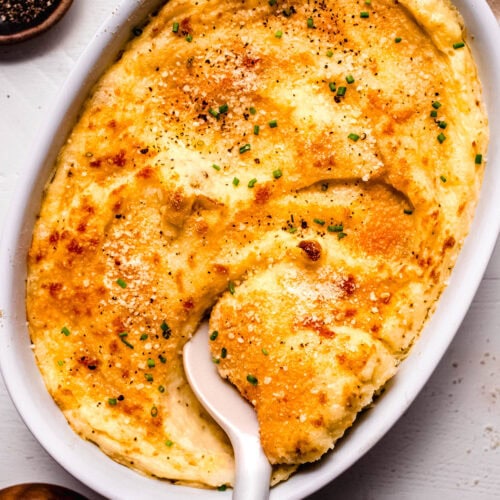 Overhead shot of finished smoked gouda mashed potatoes in baking dish with serving spoon.