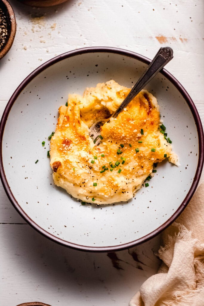 Gouda mashed potatoes in single serving dish with fork and sprinkled with chives.