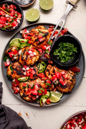 Overhead shot of pico de gallo chicken on grey plate next to small bowl of cilantro.