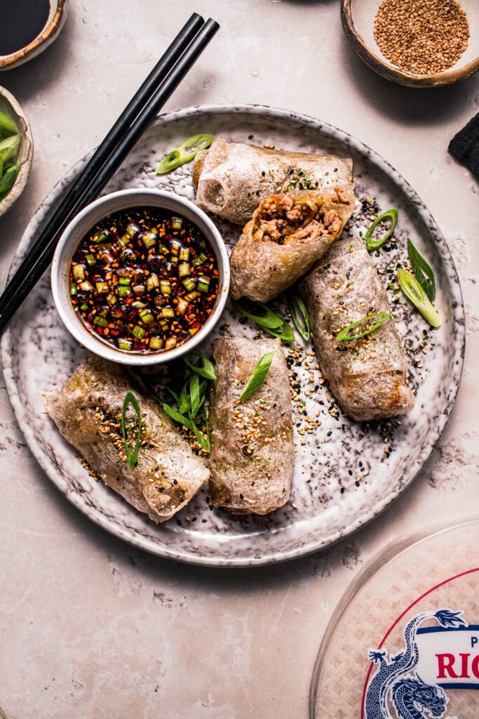 Rice paper dumplings on plate with dipping sauce and black chopsticks.
