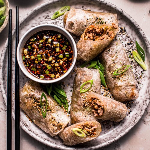 Rice paper dumplings arranged on grey plate next to small bowl of dipping sauce.