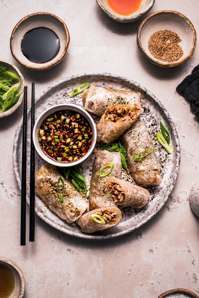 Rice paper dumplings on plate with dipping sauce and black chopsticks.