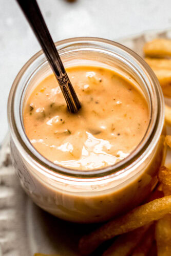 Smashburger sauce in small glass jar with spoon next to french fries.
