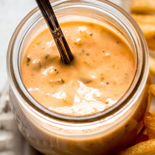 Smashburger sauce in small glass jar with spoon next to french fries.