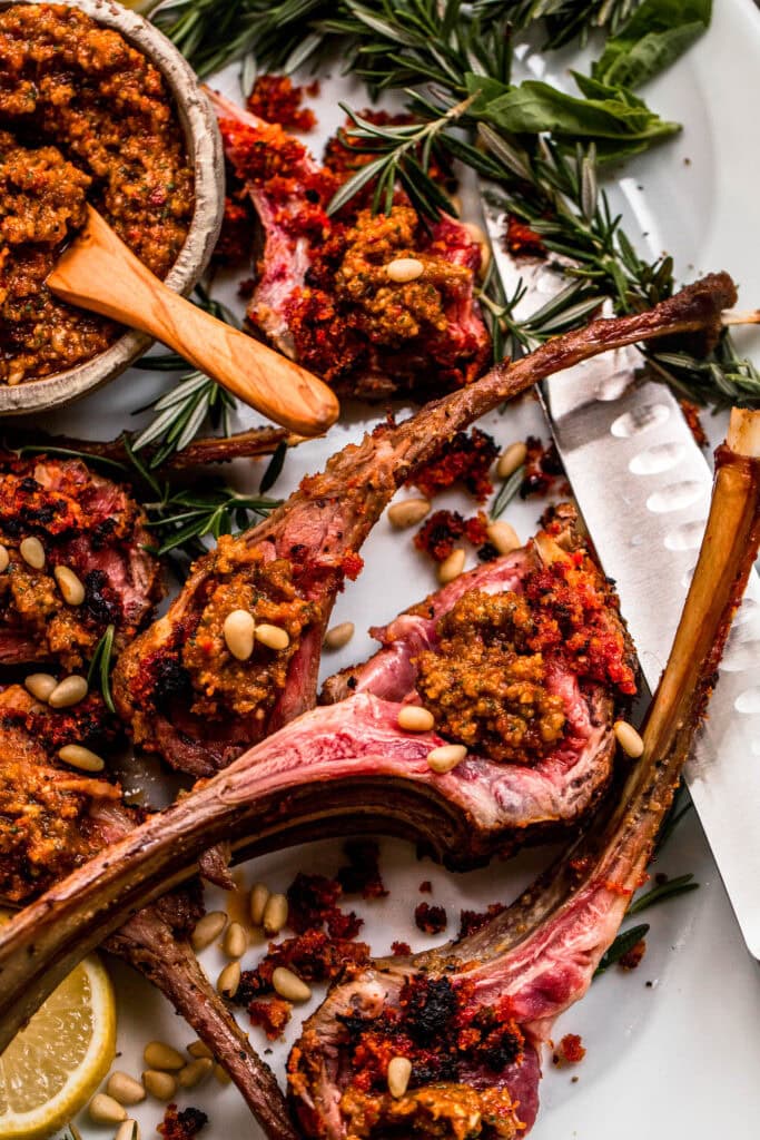 Lamb chops arranged on a serving platter, topped with sun-dried tomato pesto and served with a small bowl of pesto.