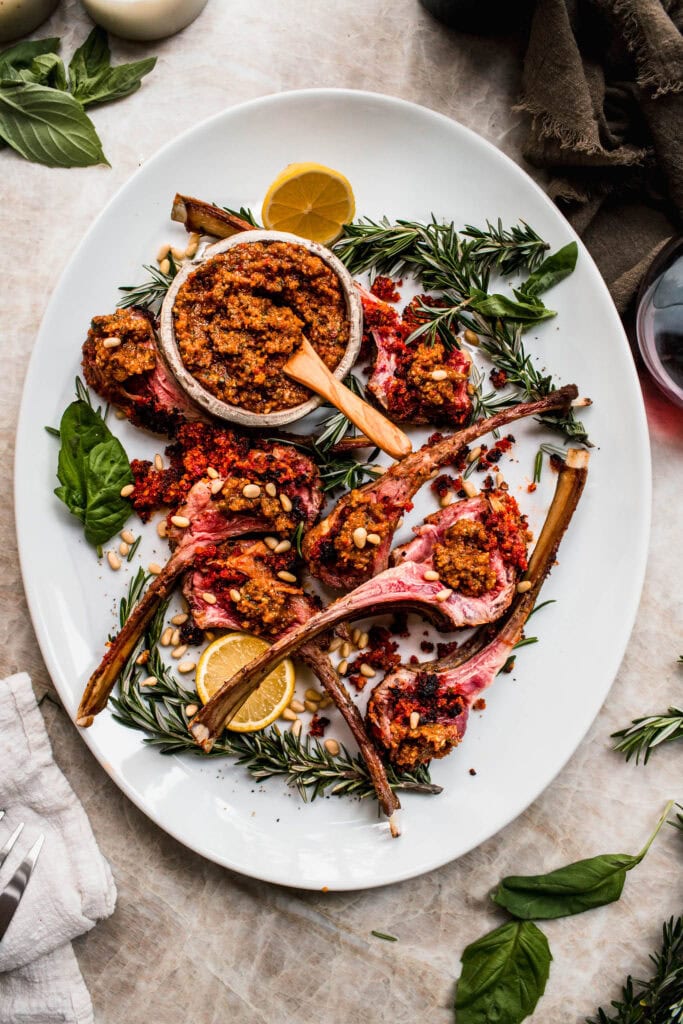 Juicy lamb chops on a platter, garnished with sun-dried tomato pesto and paired with a bowl of pesto.