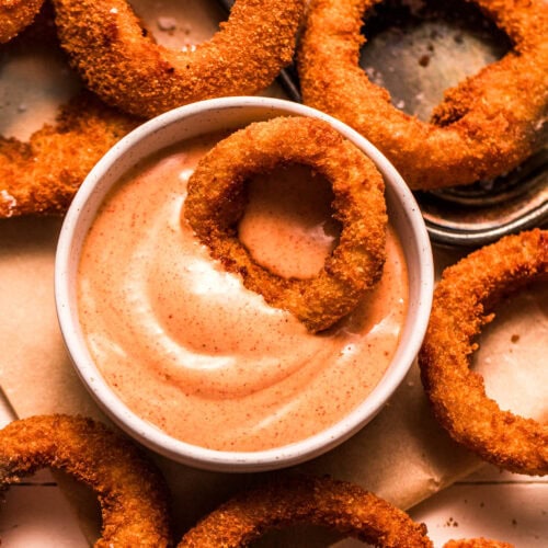 Close up of Crispy onion ring dipped into bowl of sauce.