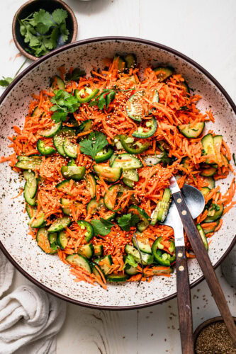 Prepared asian style carrot cucumber salad in large speckled serving bowl.