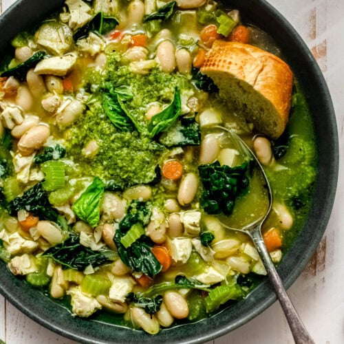 Green bowl of chicken soup with pesto, finished with a swirl of pesto and a small bowl of pesto nearby.