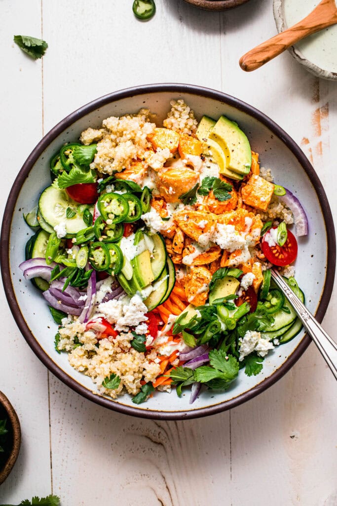 Finished buffalo chicken quinoa bowl topped with avocado, blue cheese and cilantro.