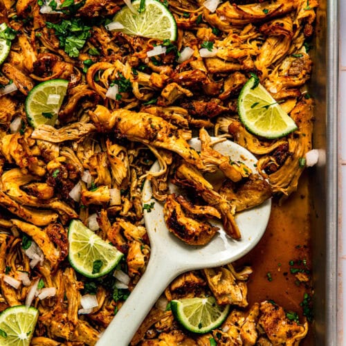 Shredded chicken carnitas on baking sheet with lime wedges and cilantro.