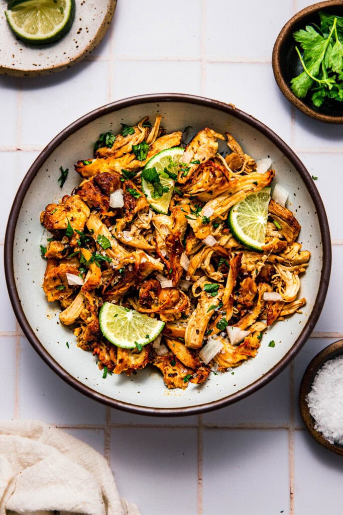 Bowl of chicken carnitas topped with lime wedges and cilantro.