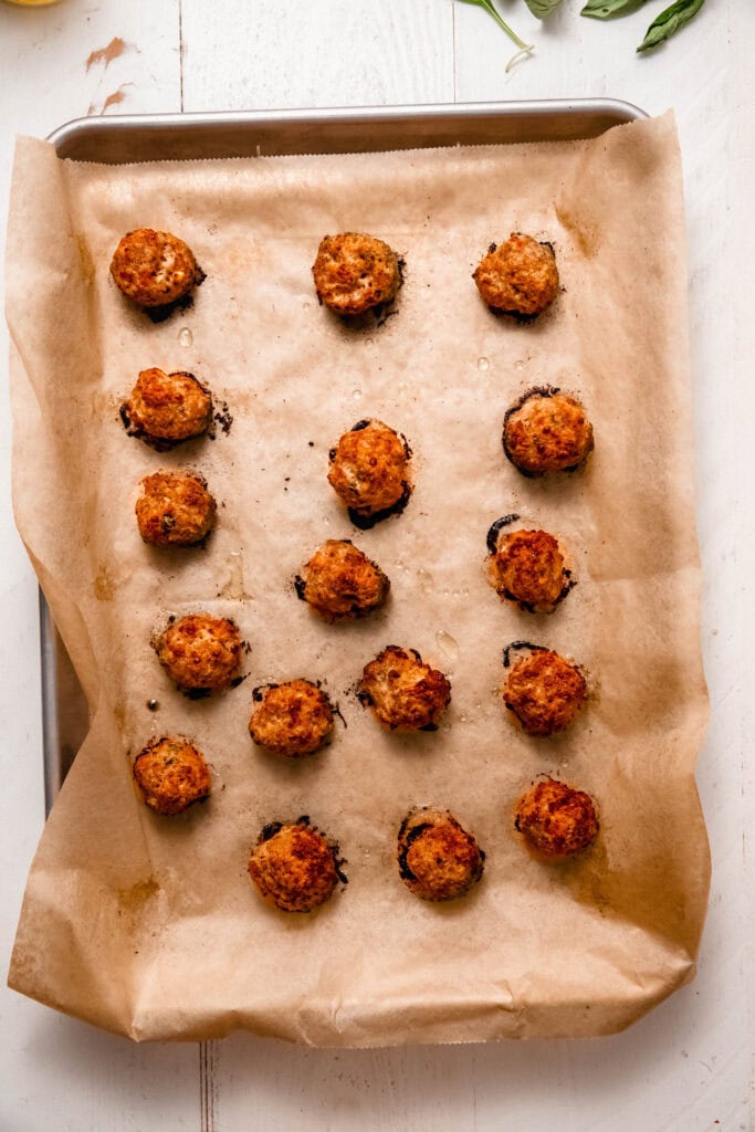 Baked chicken ricotta meatballs on baking sheet.