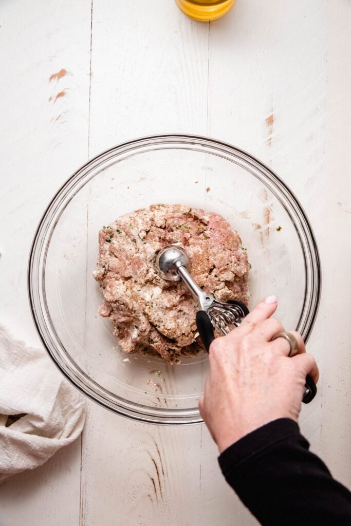 Hand scooping chicken mixture to make meatballs.