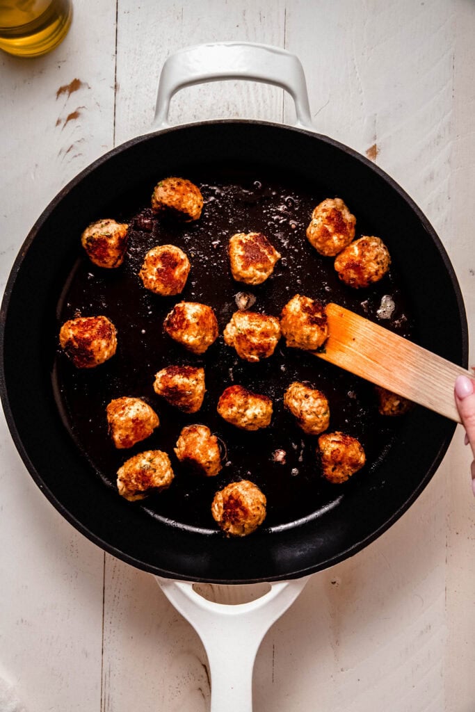 Chicken meatballs browning in skillet.