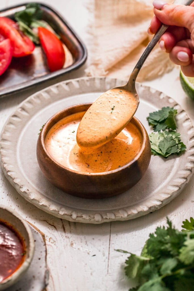 Hand dipping spoon into small bowl of chipotle ranch sauce.