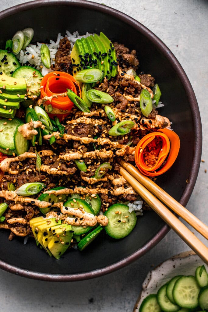 Close up of korean beef rice bowls topped with chili garlic aioli and sesame seeds.
