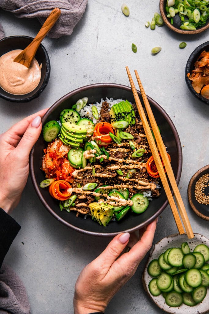 Finished korean beef bowl with toppings in black bowl with chopsticks.
